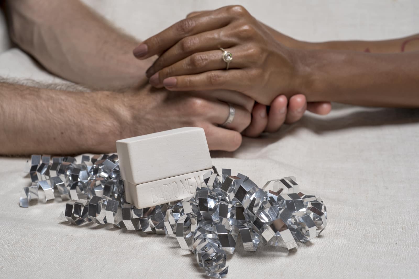Photo of couple of h ands embracing in the background with a porcelain ring box in the foreground