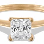 A gold engagement ring features a large, square princess-cut diamond at its center, reflecting light brilliantly. The simple band complements the diamond, highlighting its exquisite clarity in a neutral background.
