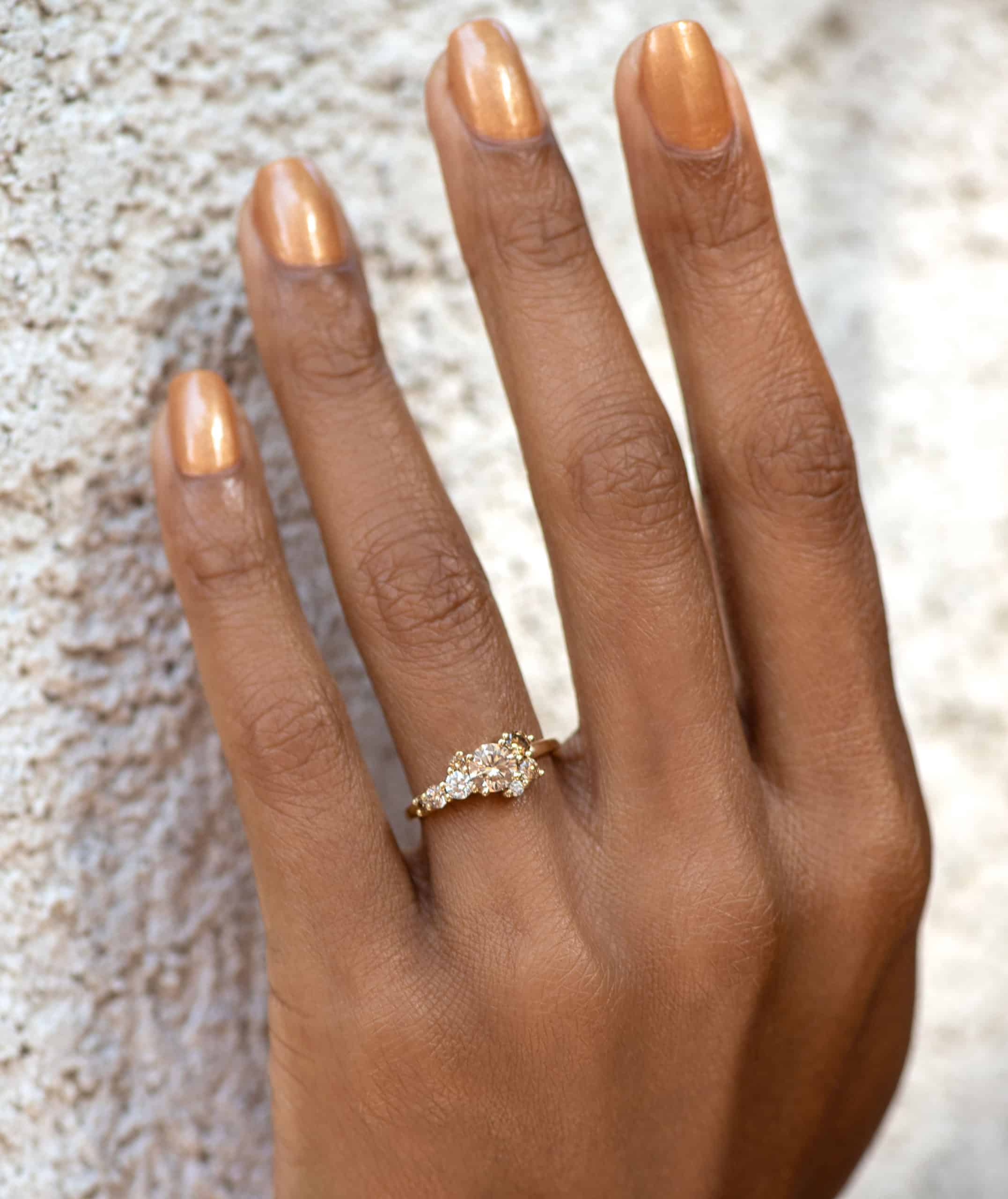 A hand with a yellow gold wedding ring set, featuring multiple sparkling stones, is positioned against a textured, light-colored wall, highlighting the ring's elegance.