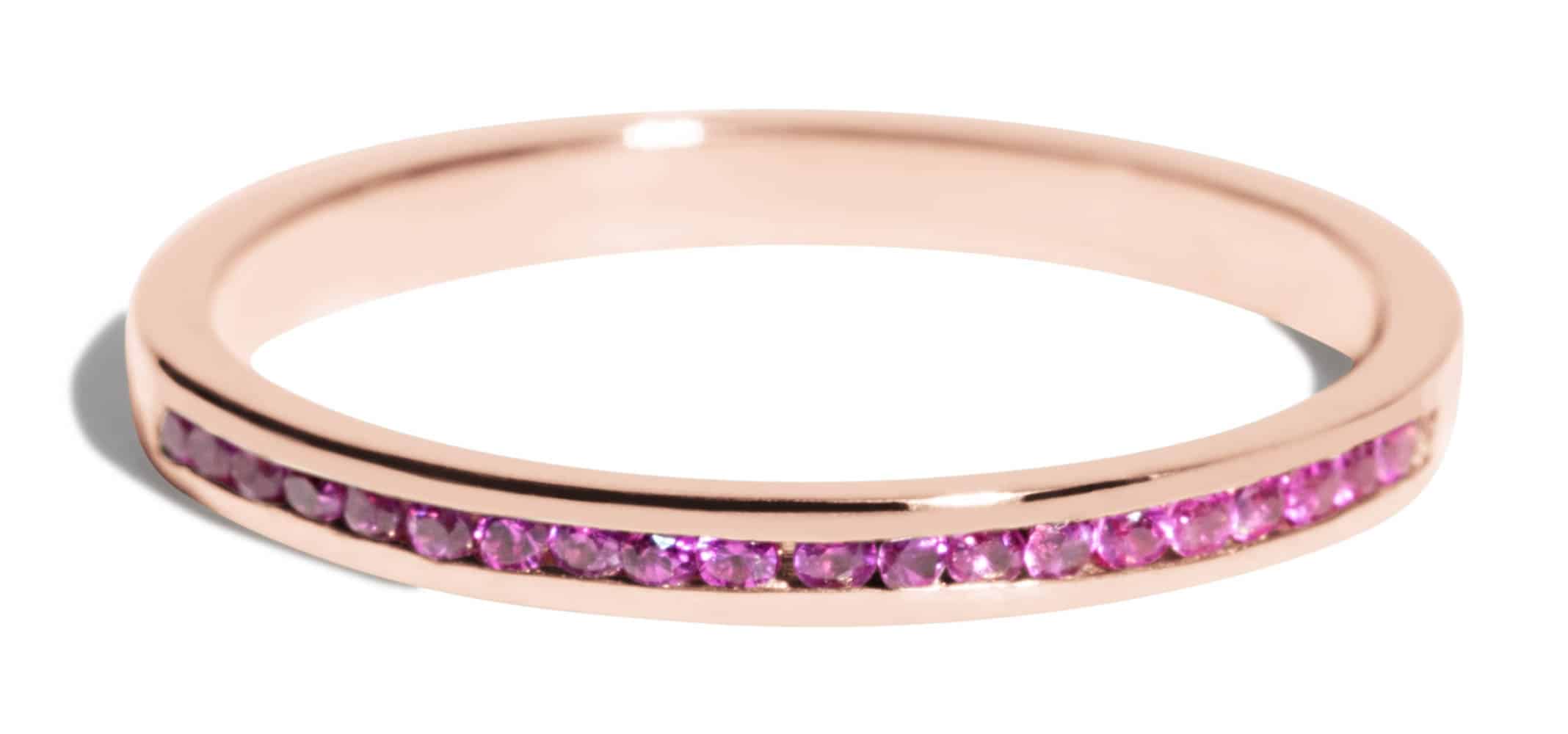 A slender rose gold engagement ring features a row of small, sparkling pink gemstones embedded along its band, reflecting light and highlighting its elegant design.