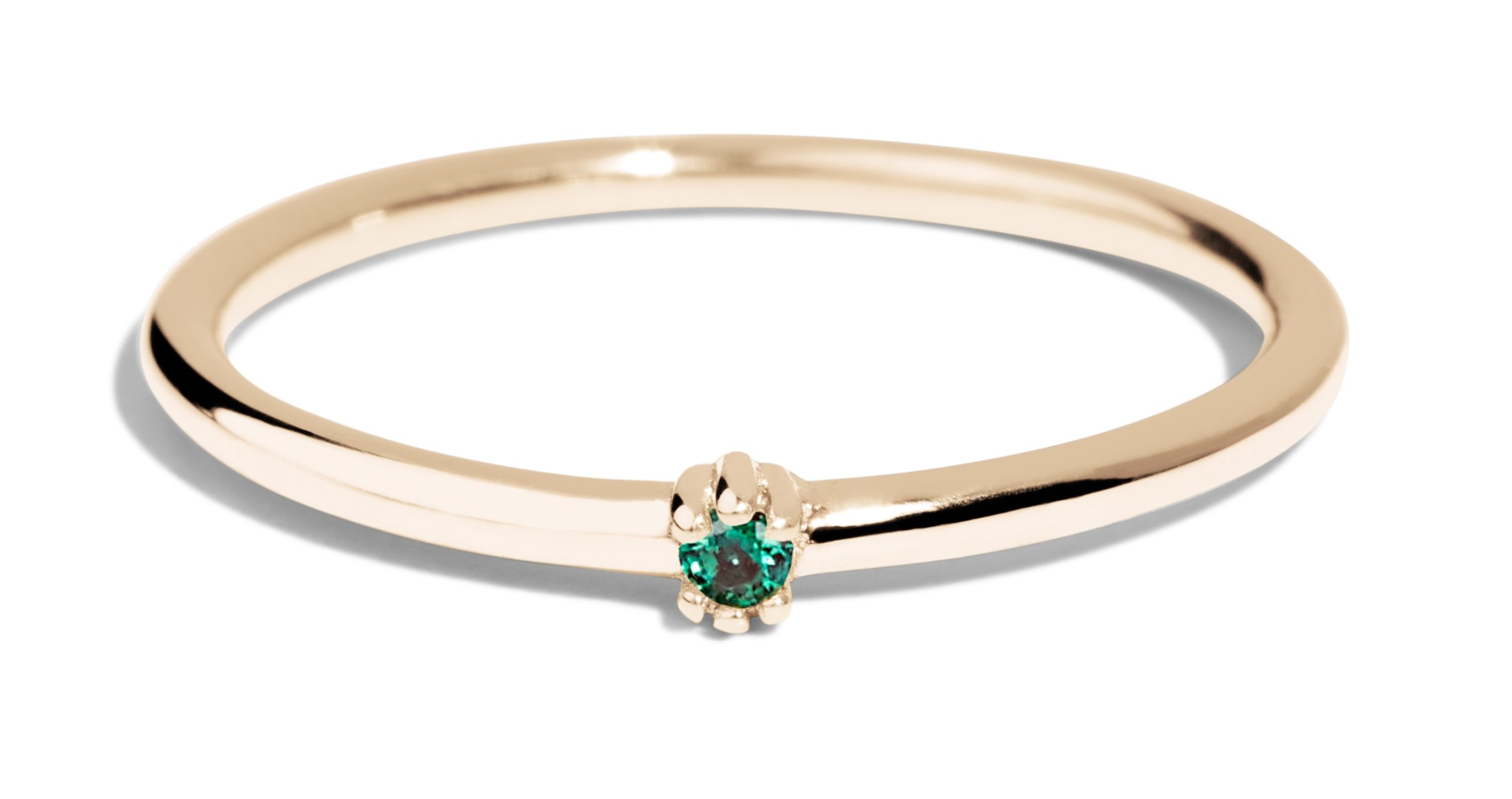 A delicate gold ring features a small, green emerald gemstone set within a claw-like design. It is displayed against a simple, light background, emphasizing its elegant shape and color.