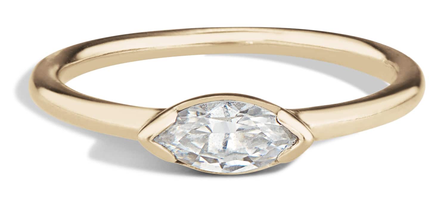 A polished yellow gold ring features an east-west set marquise diamond at its center, resting against a soft, light background that emphasizes its elegance and shine.