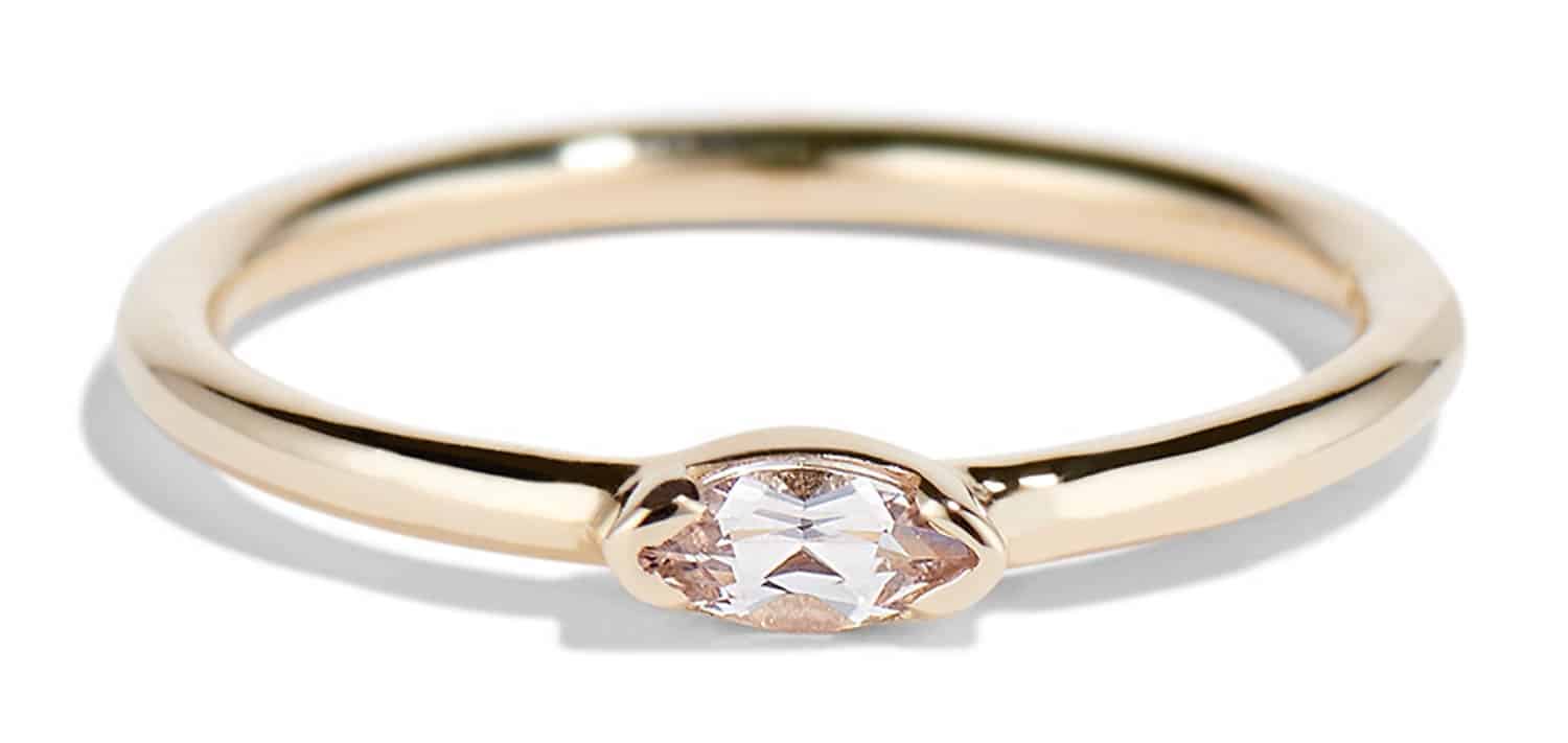 A polished gold ring features a central oval morganite solitaire, reflecting light. The pink gemstone ring rests on a soft, neutral background, emphasizing its elegance and simplicity.