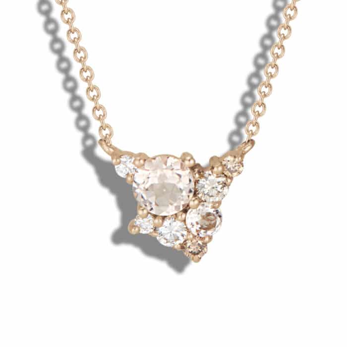 A delicate gold necklace features a triangular cluster of sparkling diamonds, showcasing a mix of round and oval-cut stones, glinting under light against a neutral background.