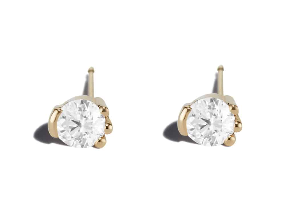 A close-up image of pair of yellow gold stud earrings, each displaying a round, brilliant-cut diamond secured by claw-like prongs, set against a plain white background.
