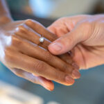Photograph of two hands holding with one hand wearing a diamond engagement ring