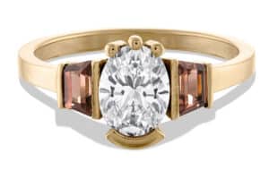 A gold ring features a large oval diamond in the center, flanked by two rectangular gemstones. The multi-shape setting is elegant, suggesting a sophisticated design intended for special occasions.