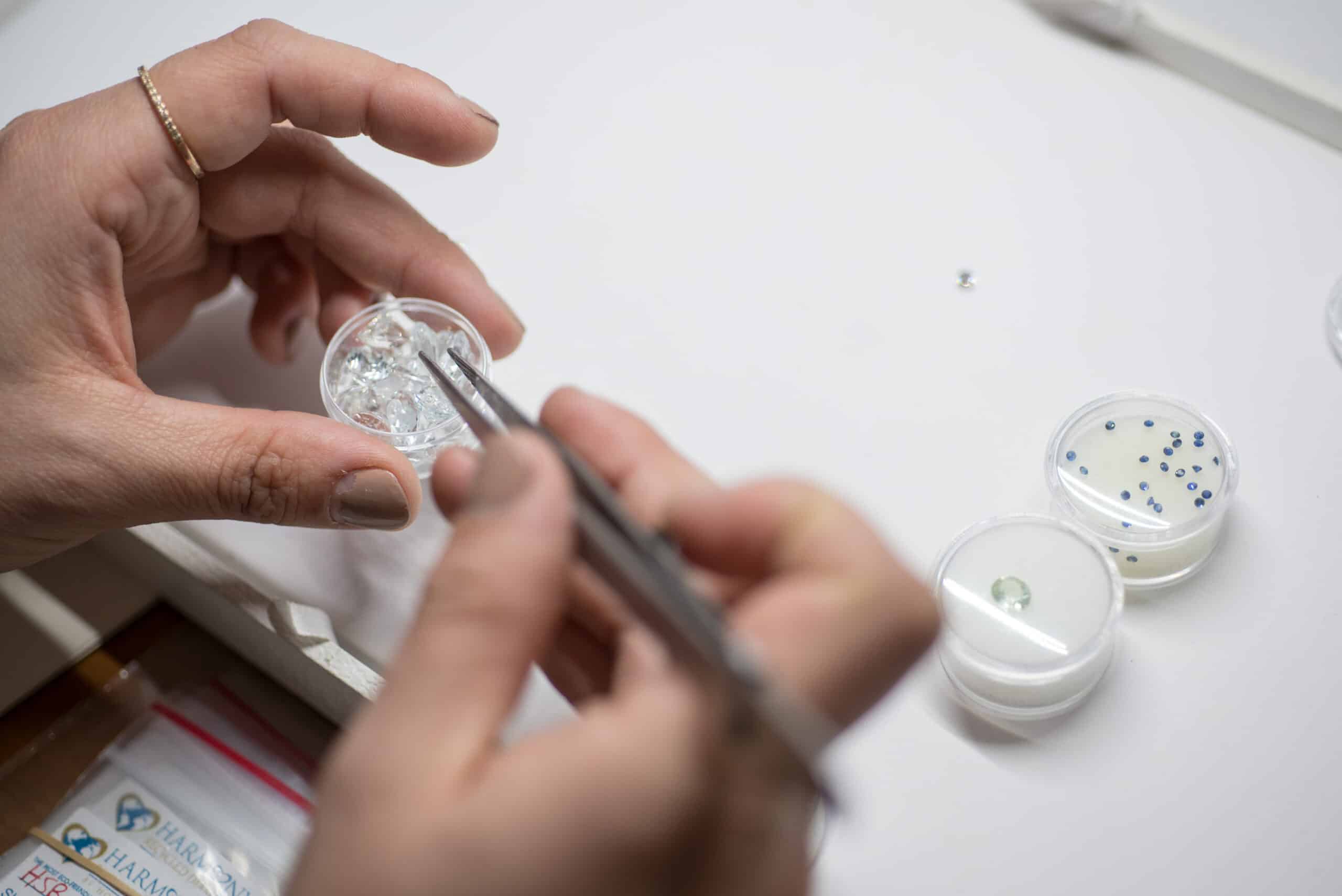 hands holding tweezers surrounded by assorted gemstones