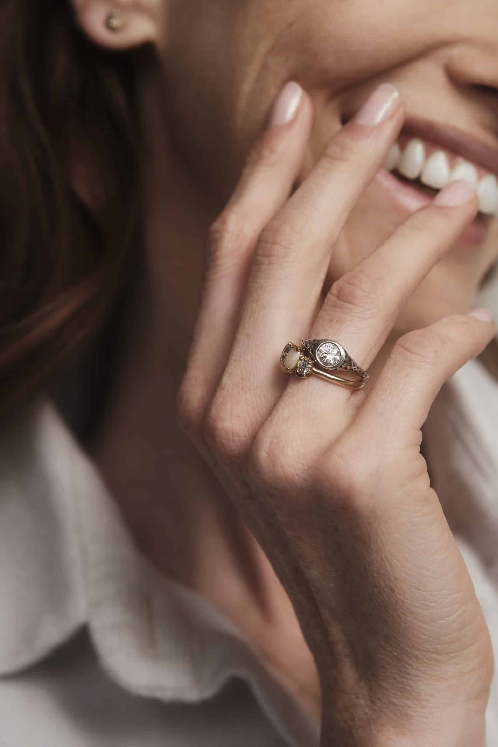woman with hand gracefully placed on cheek, showcasing a stack of rings on her ring finger.