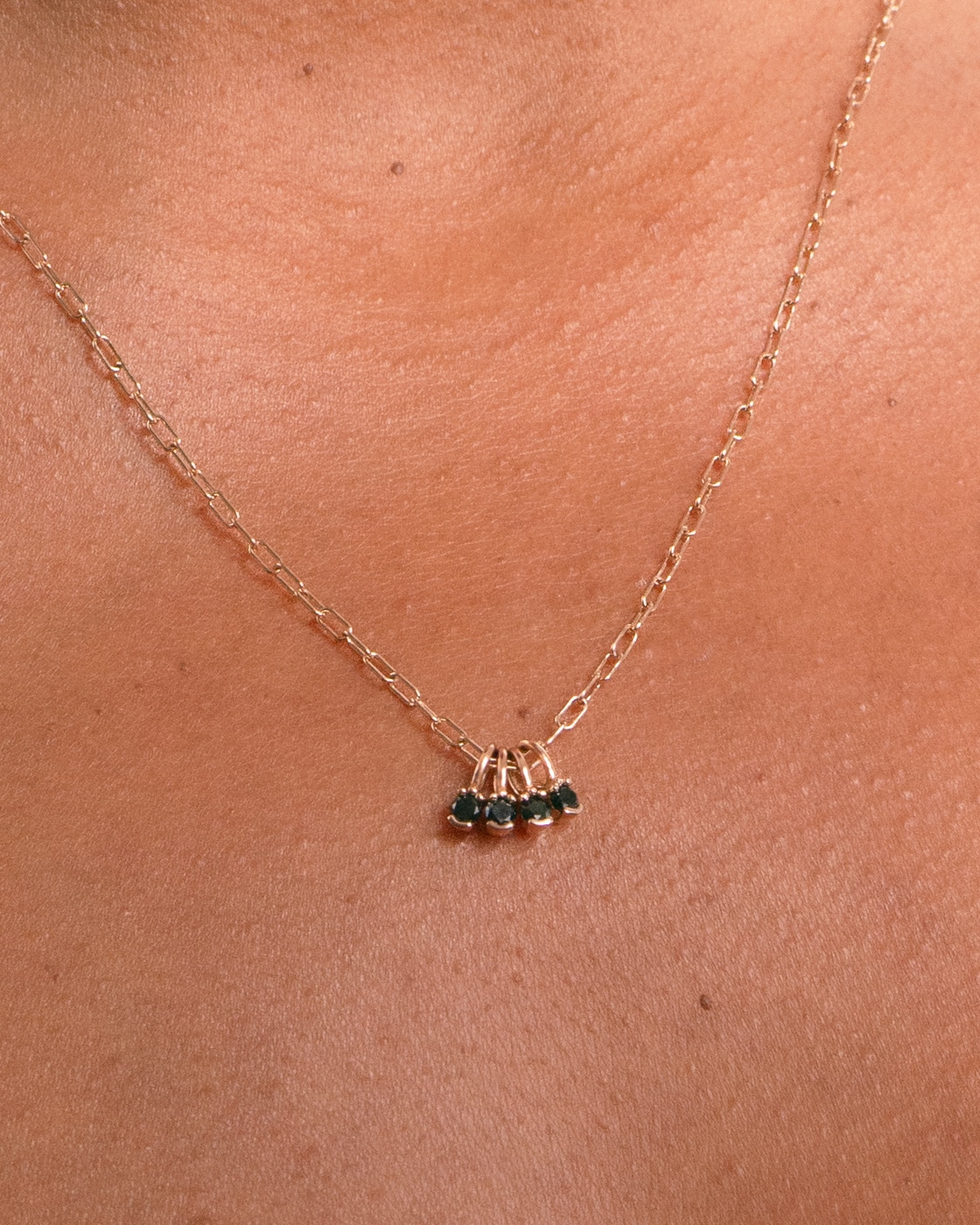 A delicate gold necklace rests on a tanned neck, featuring a series of small, dark gemstone charms clustered at the center, evoking an elegant and subtle design.