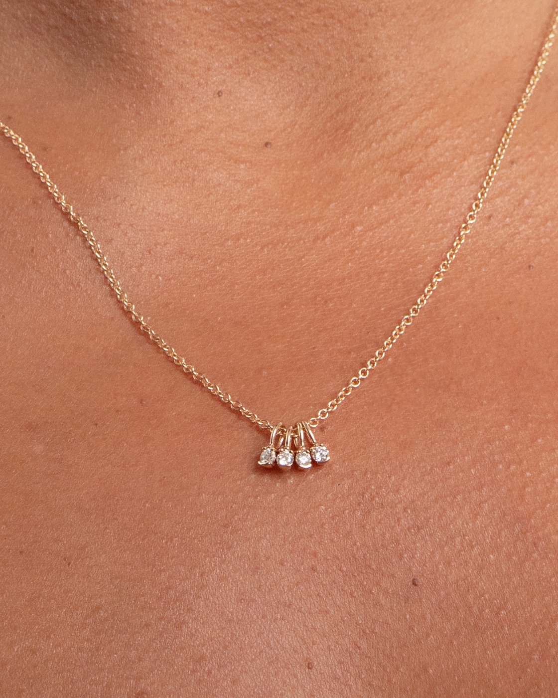 A delicate gold necklace rests on a bare neck, featuring four small, sparkling diamond pendants grouped together.