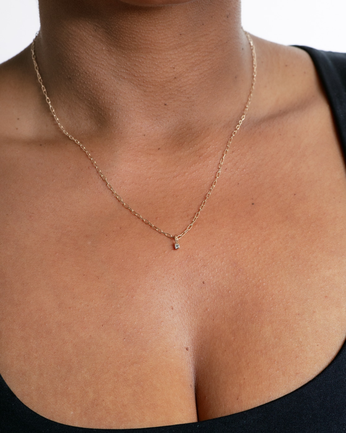 A delicate, solid gold necklace with a small diamond pendant rests on smooth skin.